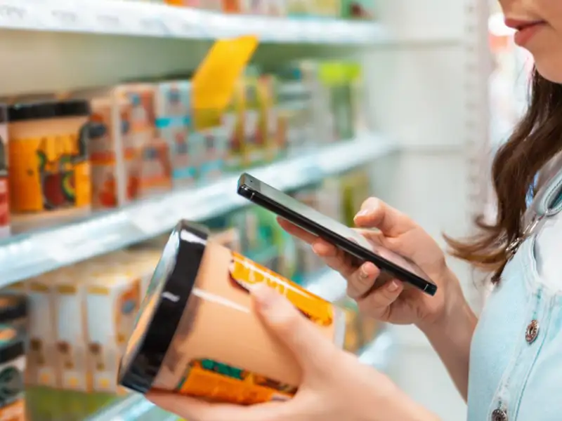 Woman shopping at a grocery store looking up product information on her cell phone.