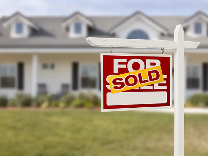 A "SOLD" marker adorns a for sale sign in front of a large residential home.