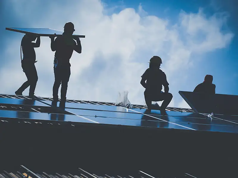 Silhouetted technicians install solar panels on a rooftop.