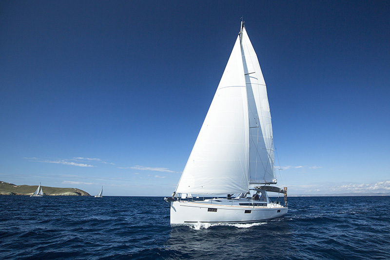 A small sailboat operates near the coast on a clear blue day.