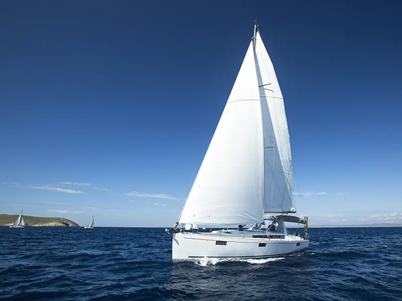 A small sailboat operates near the coast on a clear blue day.