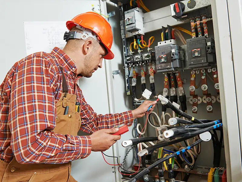 A technician uses a multi-tester on circuits in an electrical panel.