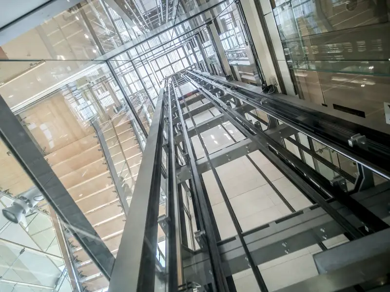 An upward view of an elevator shaft surrounded on all sides by panes of glass.