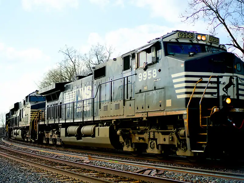 A diesel-electric train engine parked on the tracks on a bright fall day.