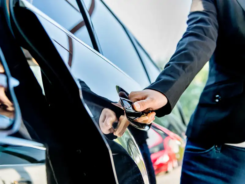 A chauffeur opens the door of a private car.