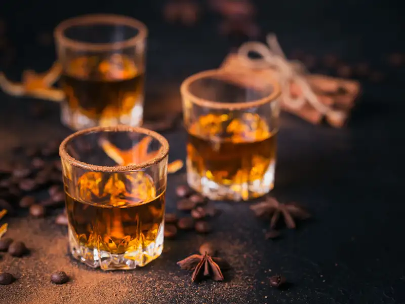 Whiskey, brandy or liquor, coffee beans, spices and decorations on dark background.
