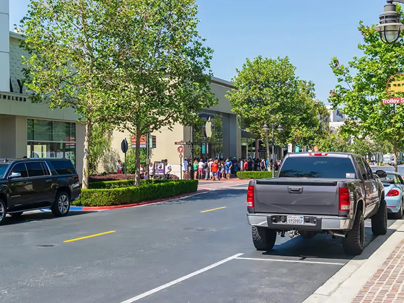Street view of a shopping district with patron lined up outside an establishment.
