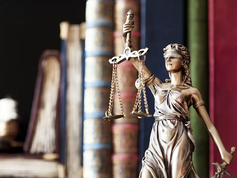 A statue of the scales of justice with law books in the background.