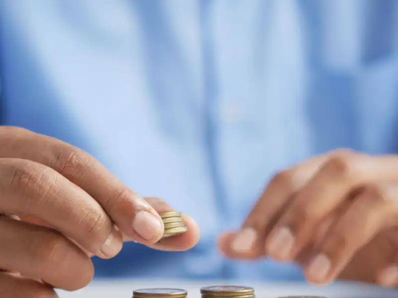 Closeup of a man wearing a blue shirt stacking coins on a table.