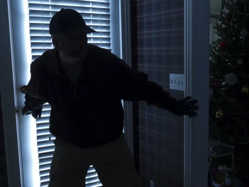 Burgler breaking into house at night during Christmas time.