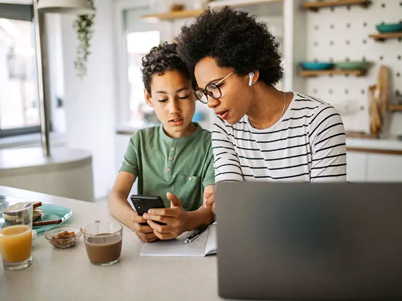 A mother an son look at information on a mobile device over breakfast at the kitchen counter.