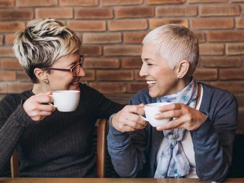 Two women sitting, laughing in a coffee shop.