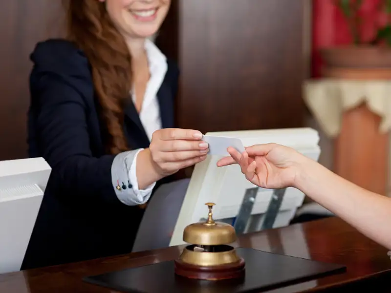 A clerk checks hands a hotel patron a key card.