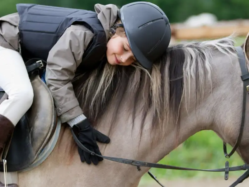 Child equestrian sitting on a horse and hugging it.