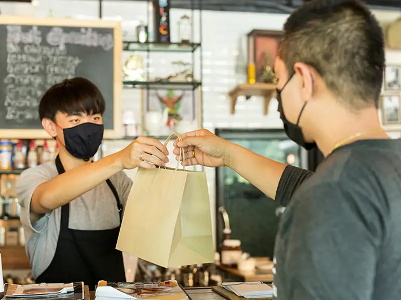 A clerk hands a patron a small paper bag over the counter.