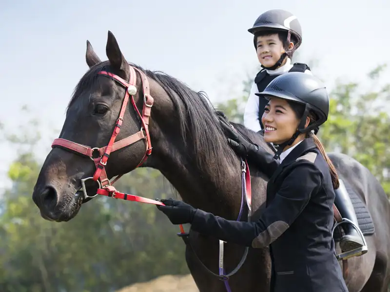 A woman guides the reigns of the horse a young child is riding.