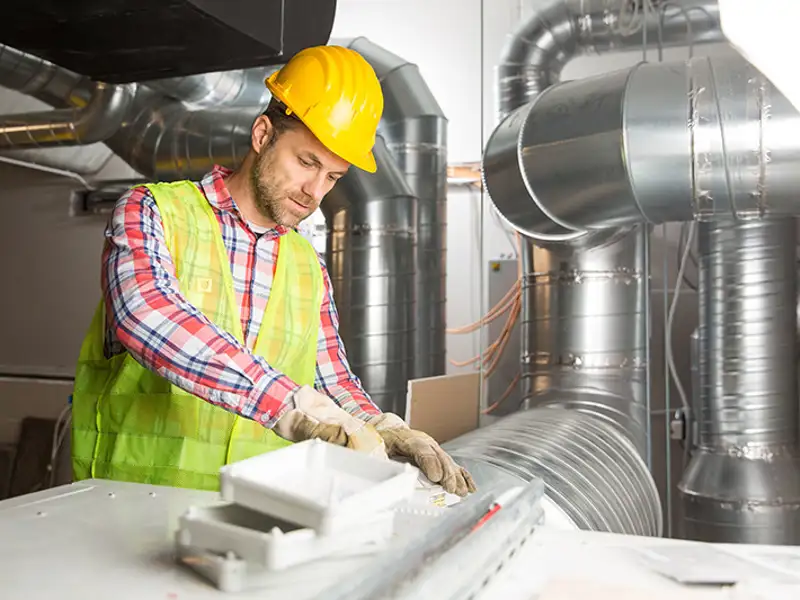 A technician in a hard works on large ventilation ducts.