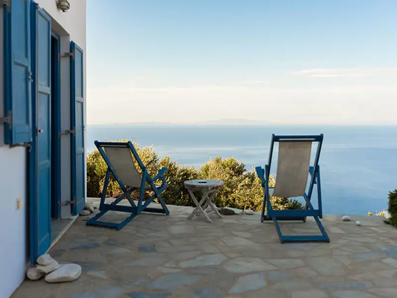 Patio chairs face a beautiful ocean view outside a quaint holiday home.