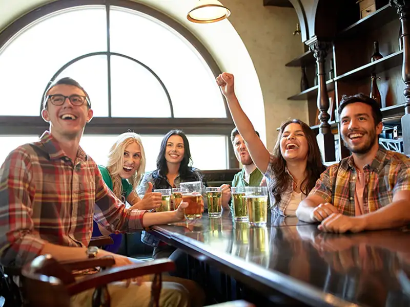 Patrons at the bar of a pub cheer while watching an event.