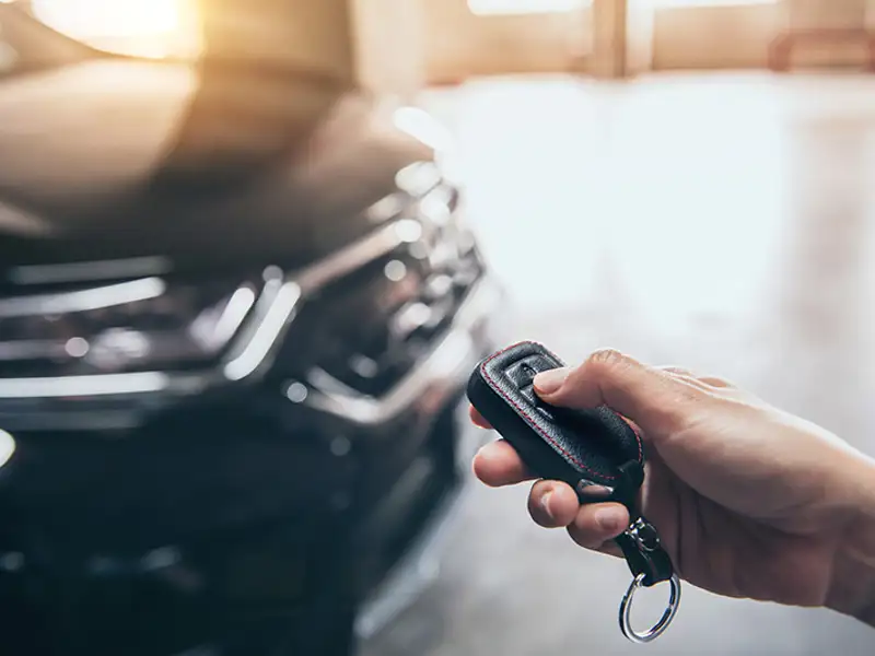 Closeup of a hand pressing the unlock button of a key fob next to a black passenger vehicle.