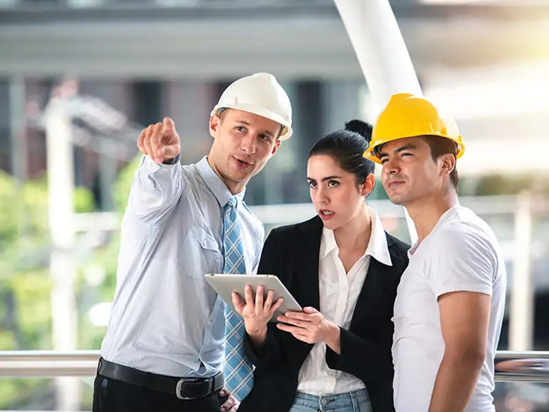A construction executive points a worker and client toward an item of interest.