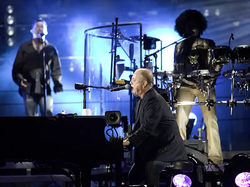 Billy Joel performs with other musicians at a concert.