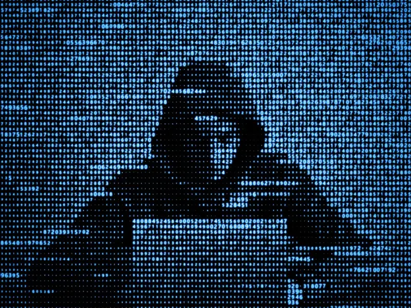 Man in hooded sweatshirt hacking on a laptop .