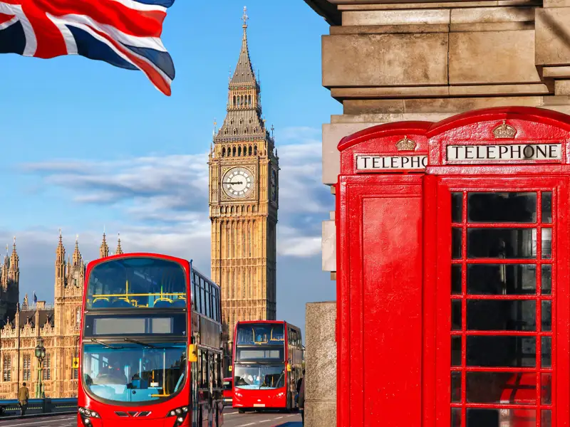Double-decker busses pass red telephone booths near Big Ben.