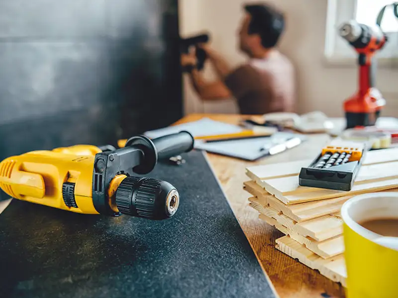 A carpenter works in the background as tools sit on a bench in the foreground.