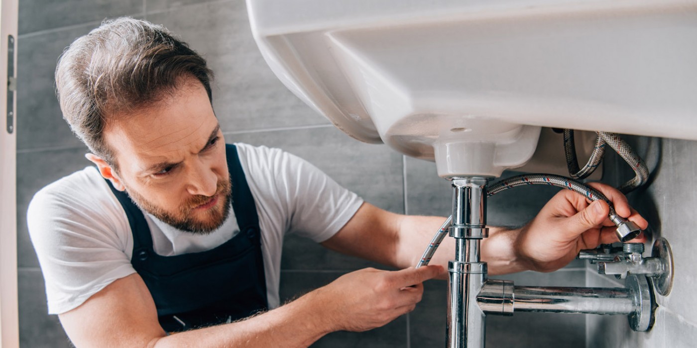 Plumber working under a residential bathroom sink.