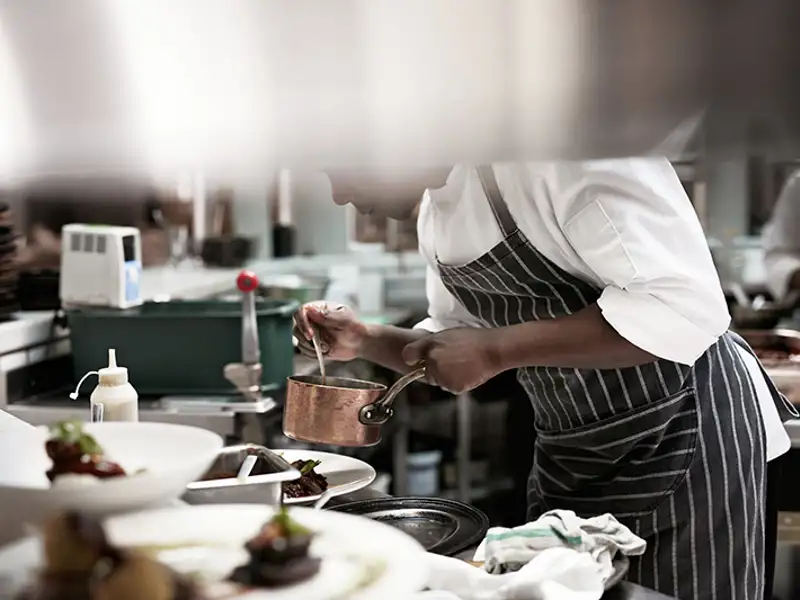 A gourmet chef prepares a sauce in a copper saucepan.