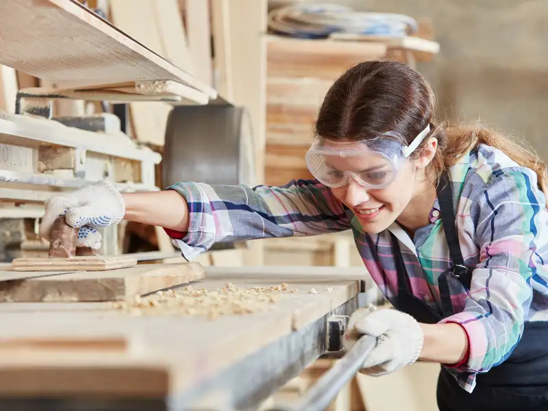 A smiling woman works in a wood shop.