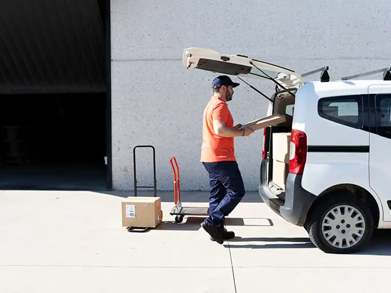 A delivery driver loads boxes into the back of a small commercial van.