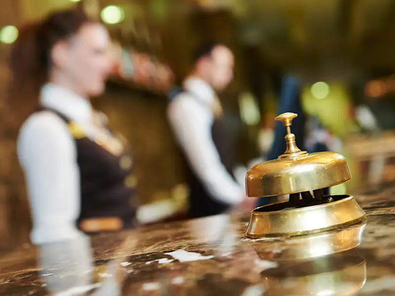 Closeup of a service bell on the marble of a hotel check-in desk with hotel workers in the background.