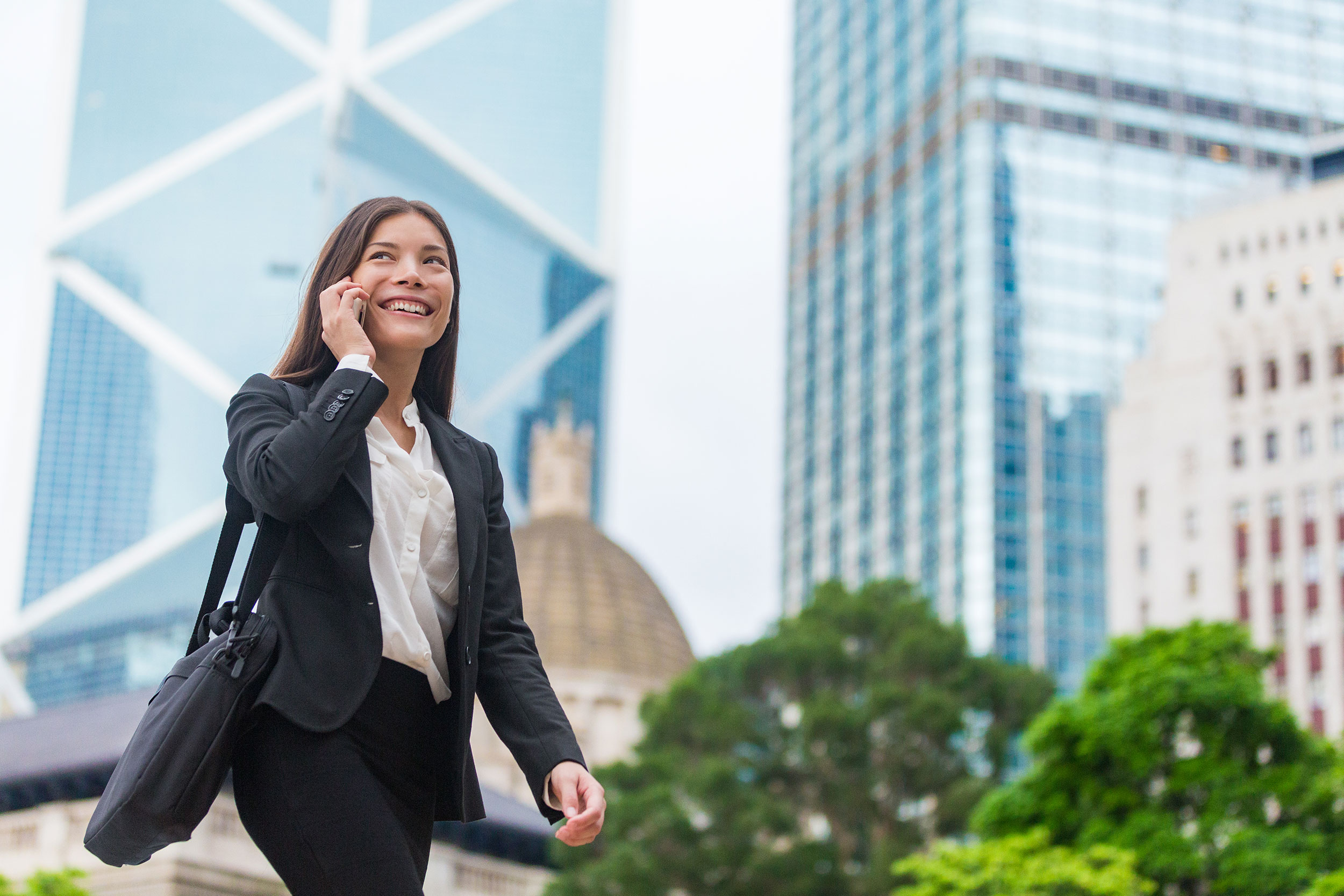 A professional walks in a sunny downtown area, speaking on a mobile device.