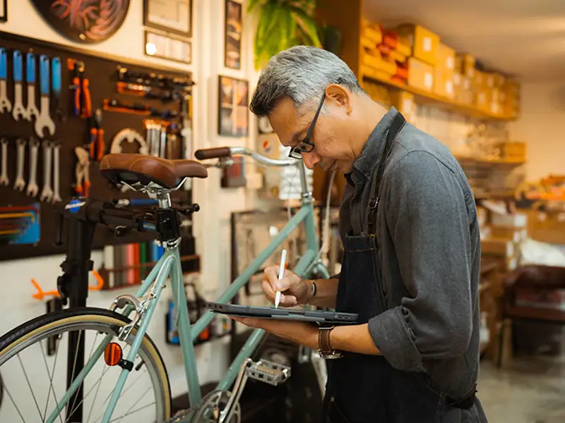 A technician references an electronic tablet before making repairs on a client's bicycle.