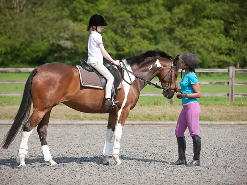 A horse riding instructor gives a lesson to a mounted student.