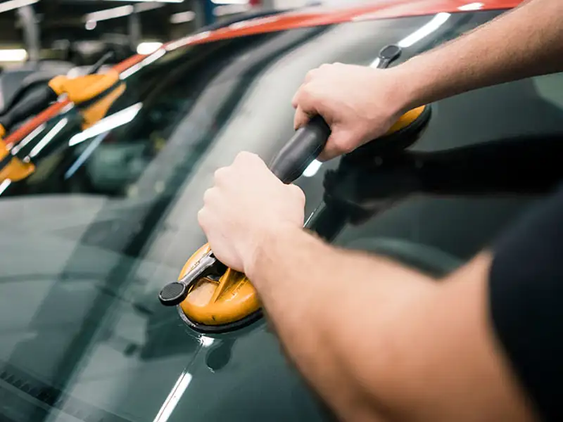 A technician installs a large pane of tinted glass on a vehicle.