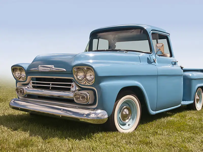 A light blue vintage pickup truck parked in a sunny meadow.
