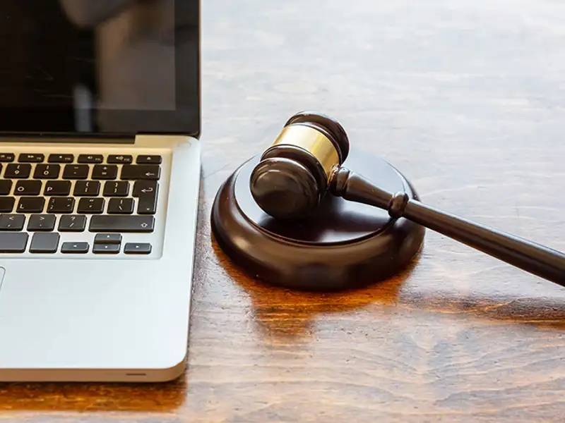 A gavel sits next to a laptop on a wooden desk.