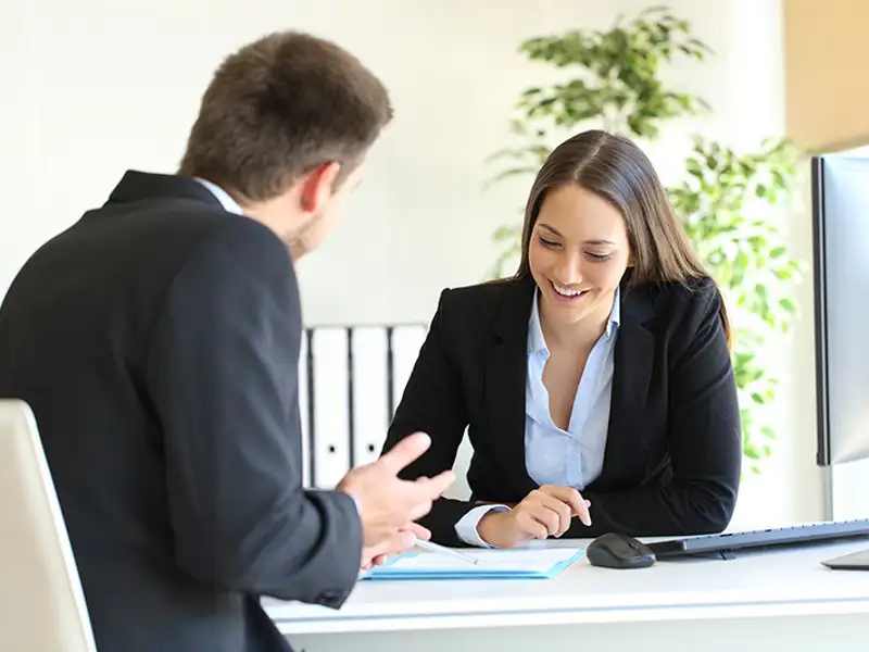 A smiling man and woman in business attire discuss a contract at a desk.