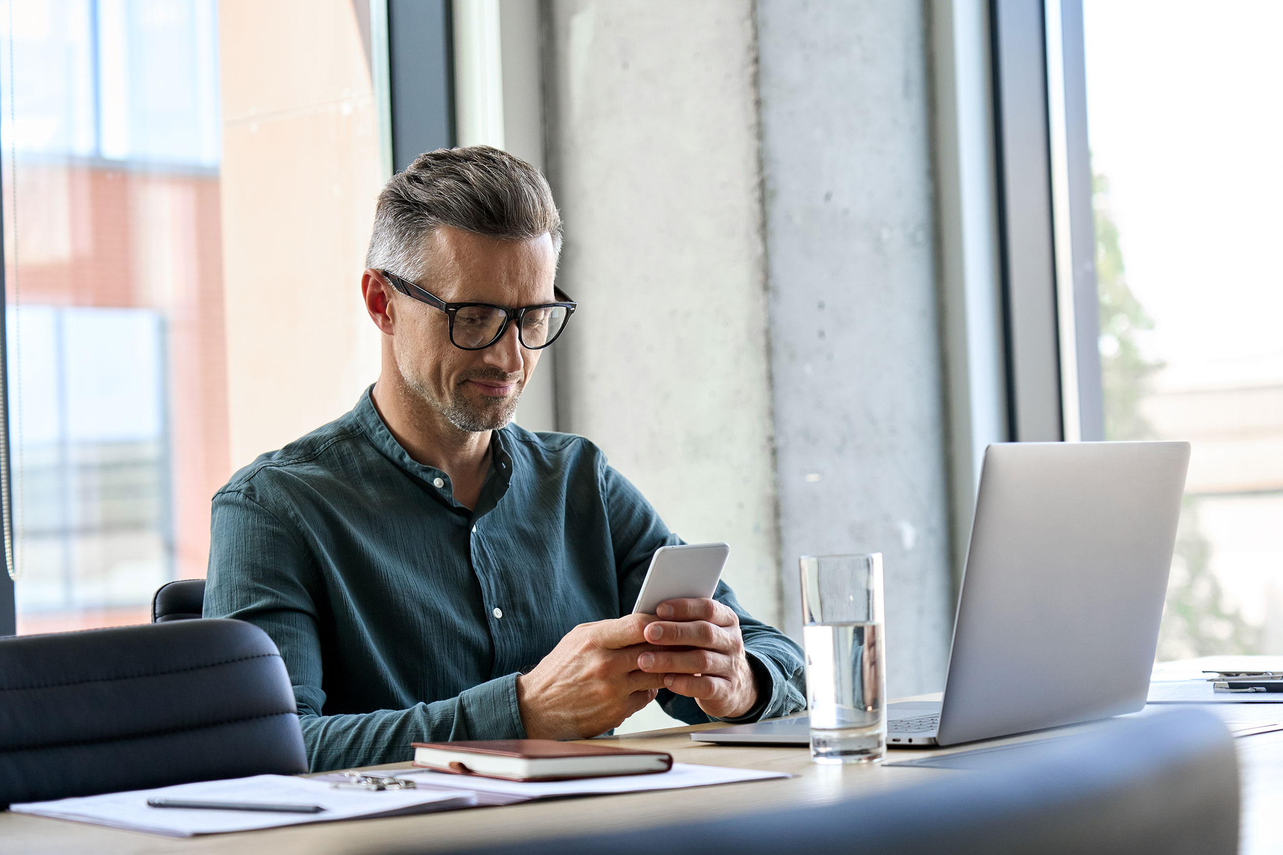 A mature man with glasses smiles as he looks at information on a mobile device.